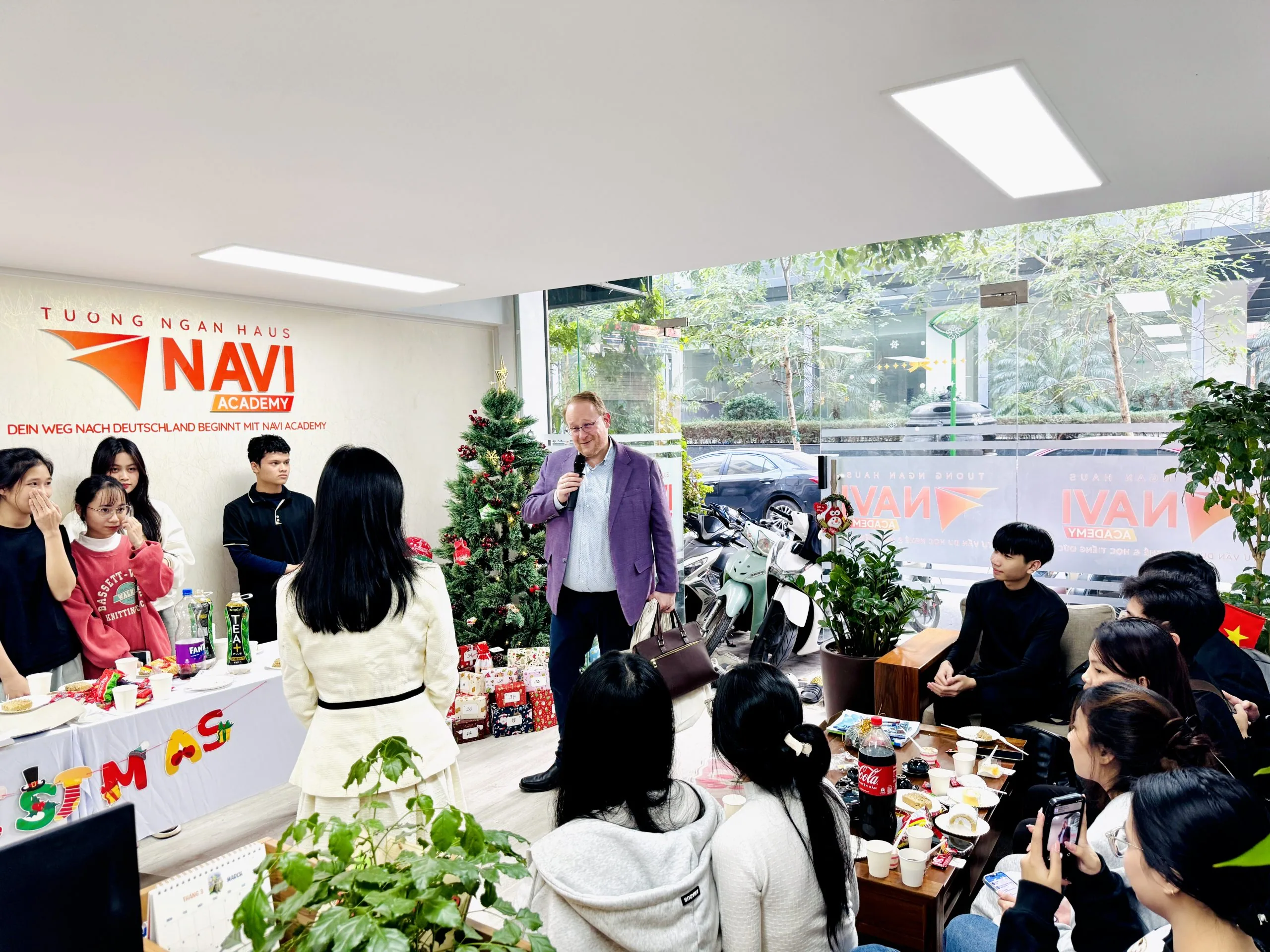 Tiến sĩ Steffen Kaupp cầm micro chia sẻ với học viên NAVI Academy bên cây thông Noel trong buổi tiệc Giáng sinh.