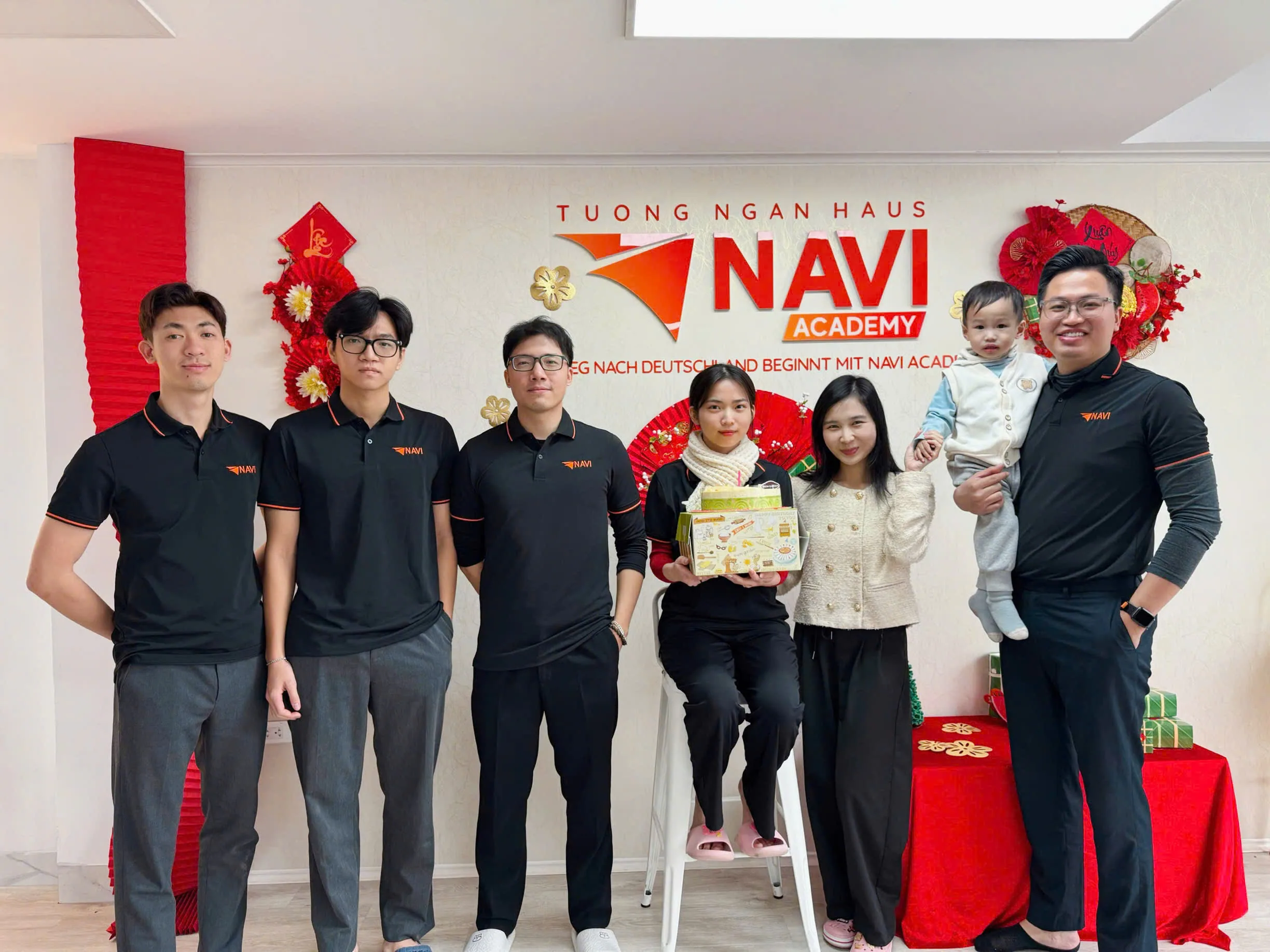 Đội ngũ NAVI Academy mặc áo đồng phục đen chụp ảnh cùng nhau dịp Tết bên bàn quà.