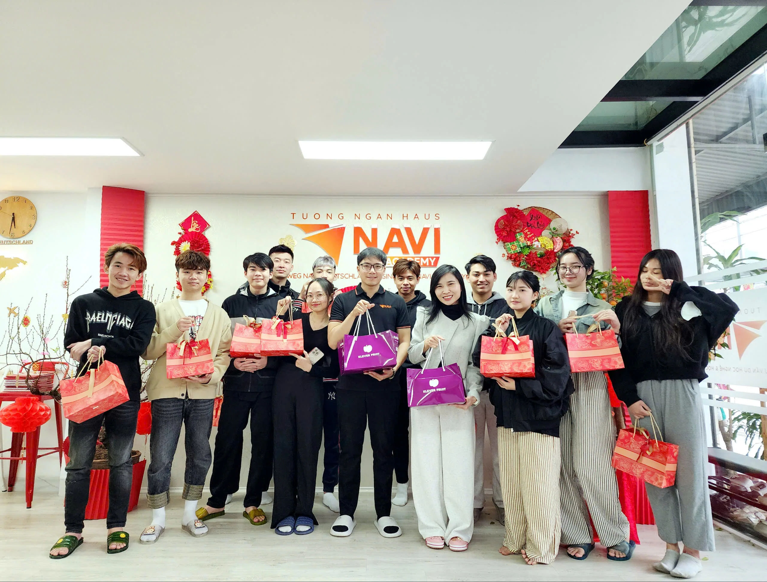 Nhóm học viên và nhân viên NAVI Academy cầm túi quà Tết, chụp ảnh trước bảng hiệu trung tâm.